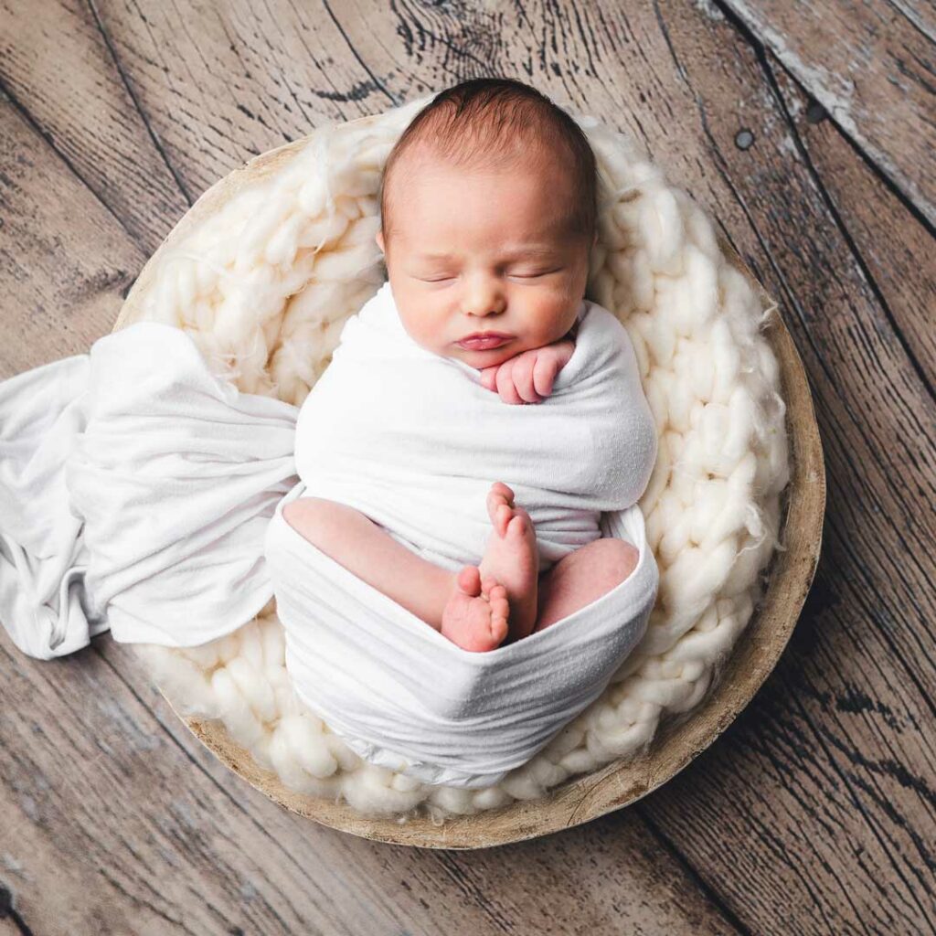 A newborn baby sleeps soundly in a white basket